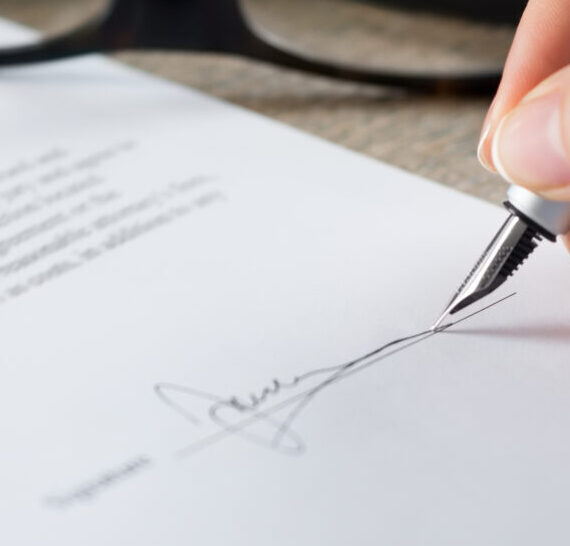 Closeup shot of a woman signing a form. She's writing on a financial contract. Shallow depth of field with focus on tip of the pen.